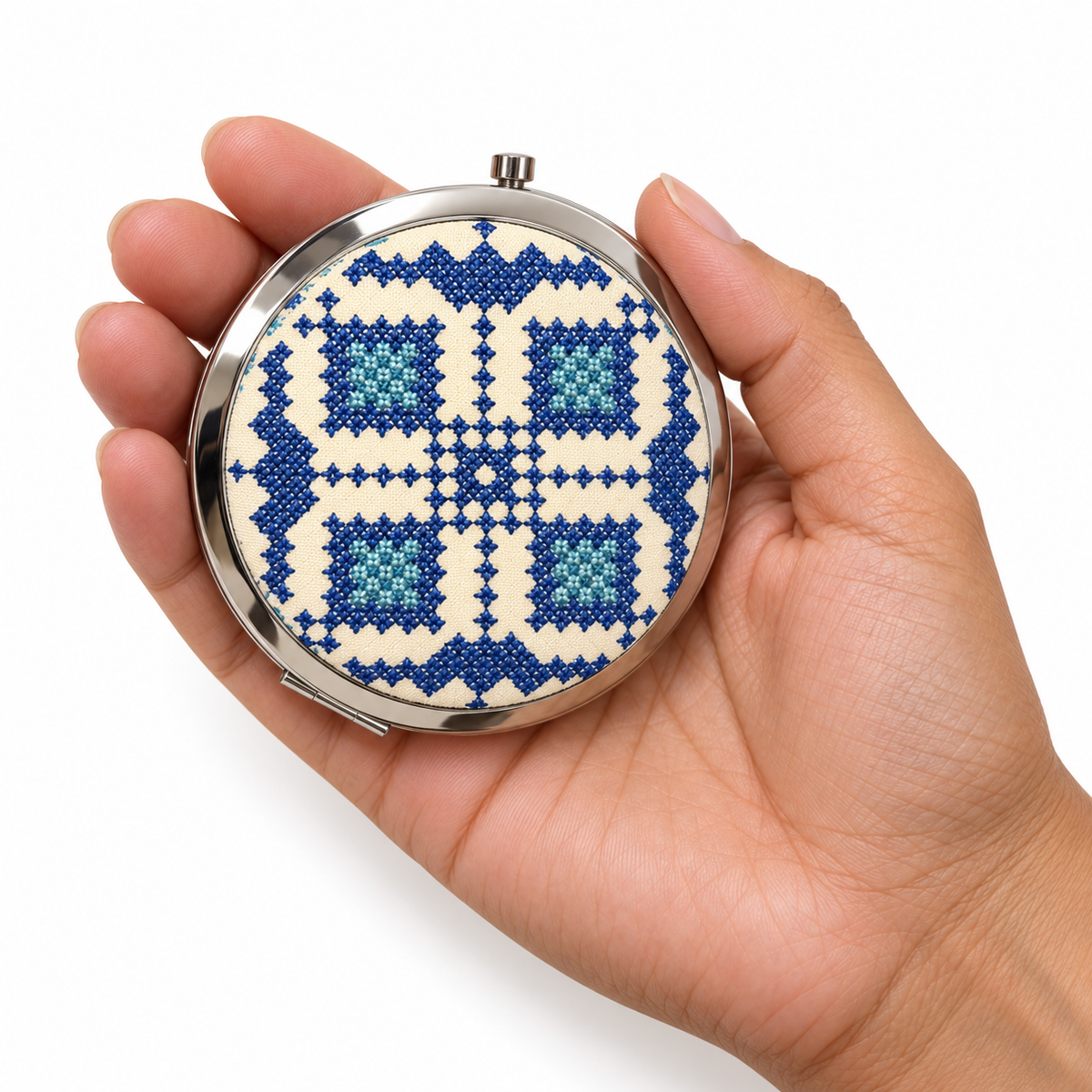 Representative tatreez pocket mirror held in a model’s hand on a white background. Patterns and colours vary.